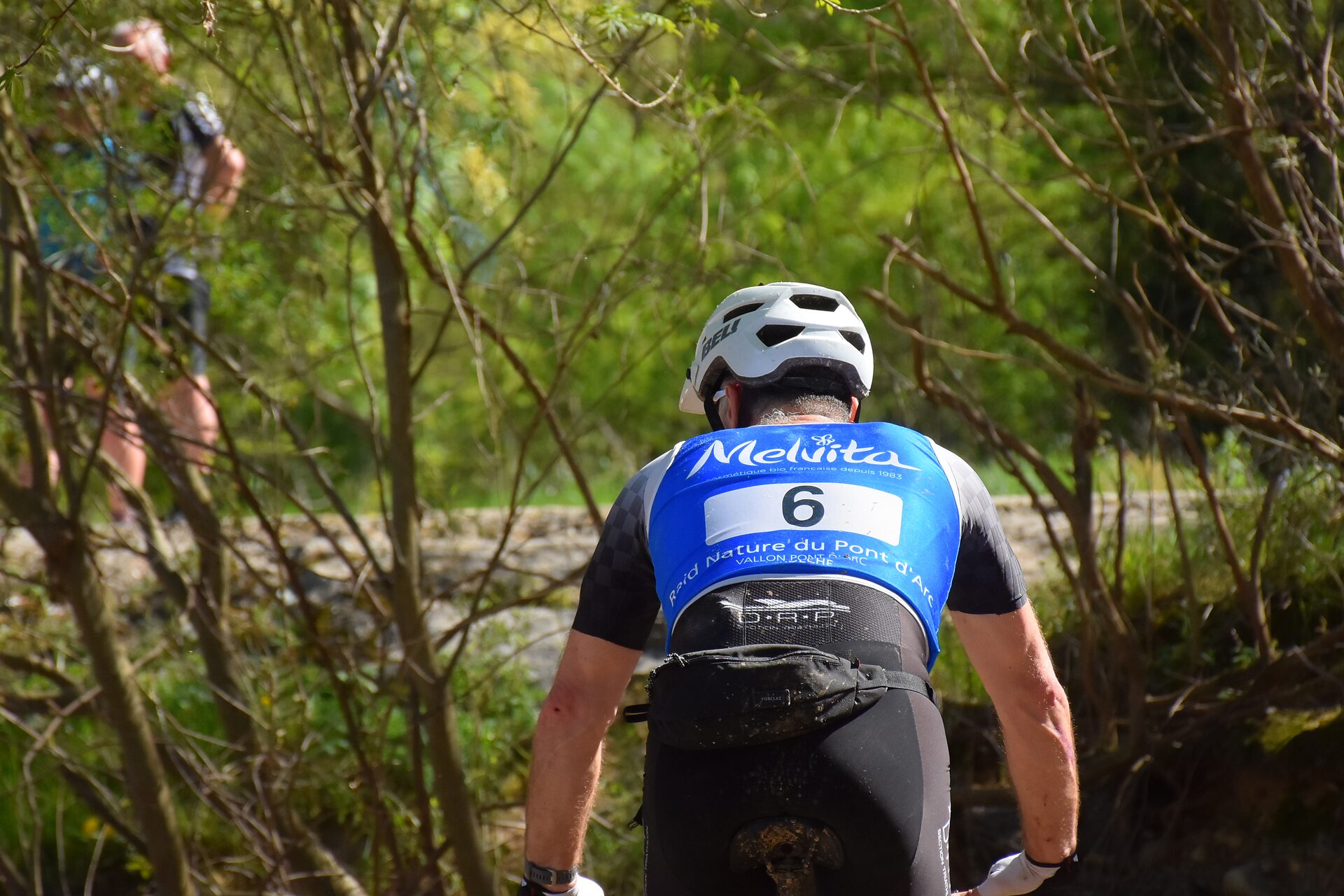 Vététiste de dos arborant un dossard partenaire lors du raid nature en Ardèche à Vallon
